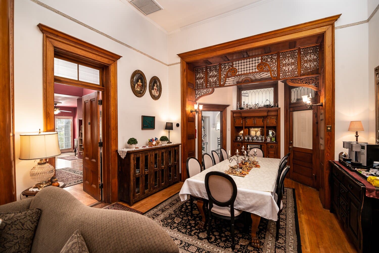A warmly decorated dining area featuring a large table, elegant chairs, and wooden accents, adjacent to a cozy living space.