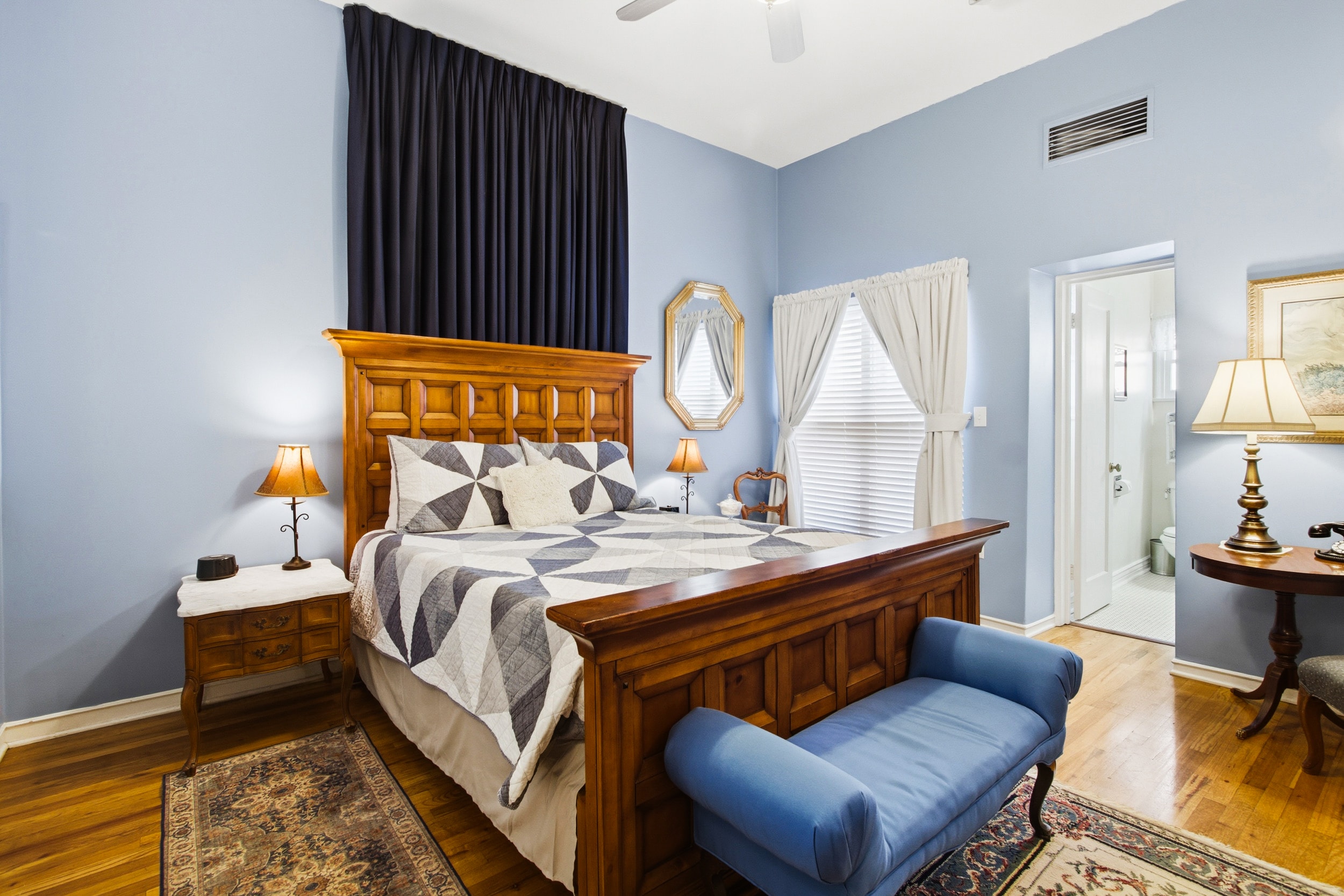Cozy bedroom featuring a wooden bed with a quilt, a blue bench, and light blue walls.