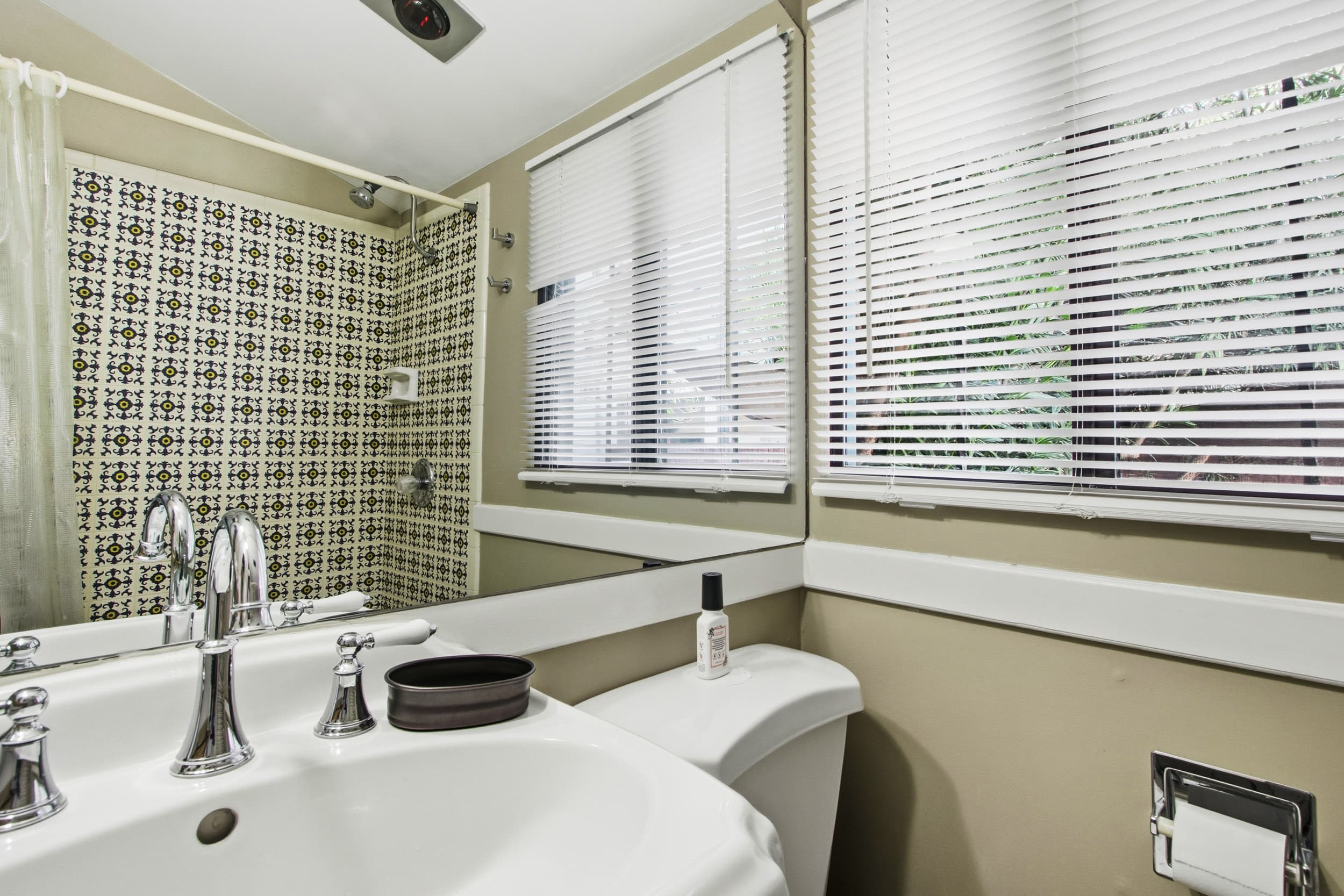 A modern bathroom featuring a patterned shower wall, sink with chrome fixtures, and natural light from blinds.