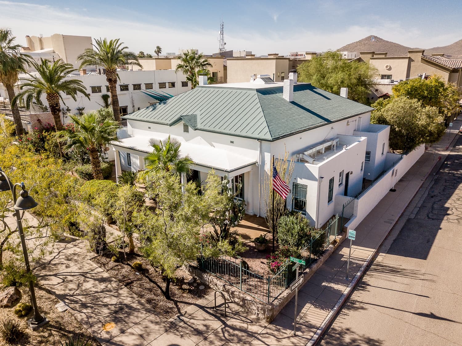 Aerial view of a white house with a green roof surrounded by palm trees and a walkway. Aerial view of a white house with a green roof surrounded by palm trees and a walkway.