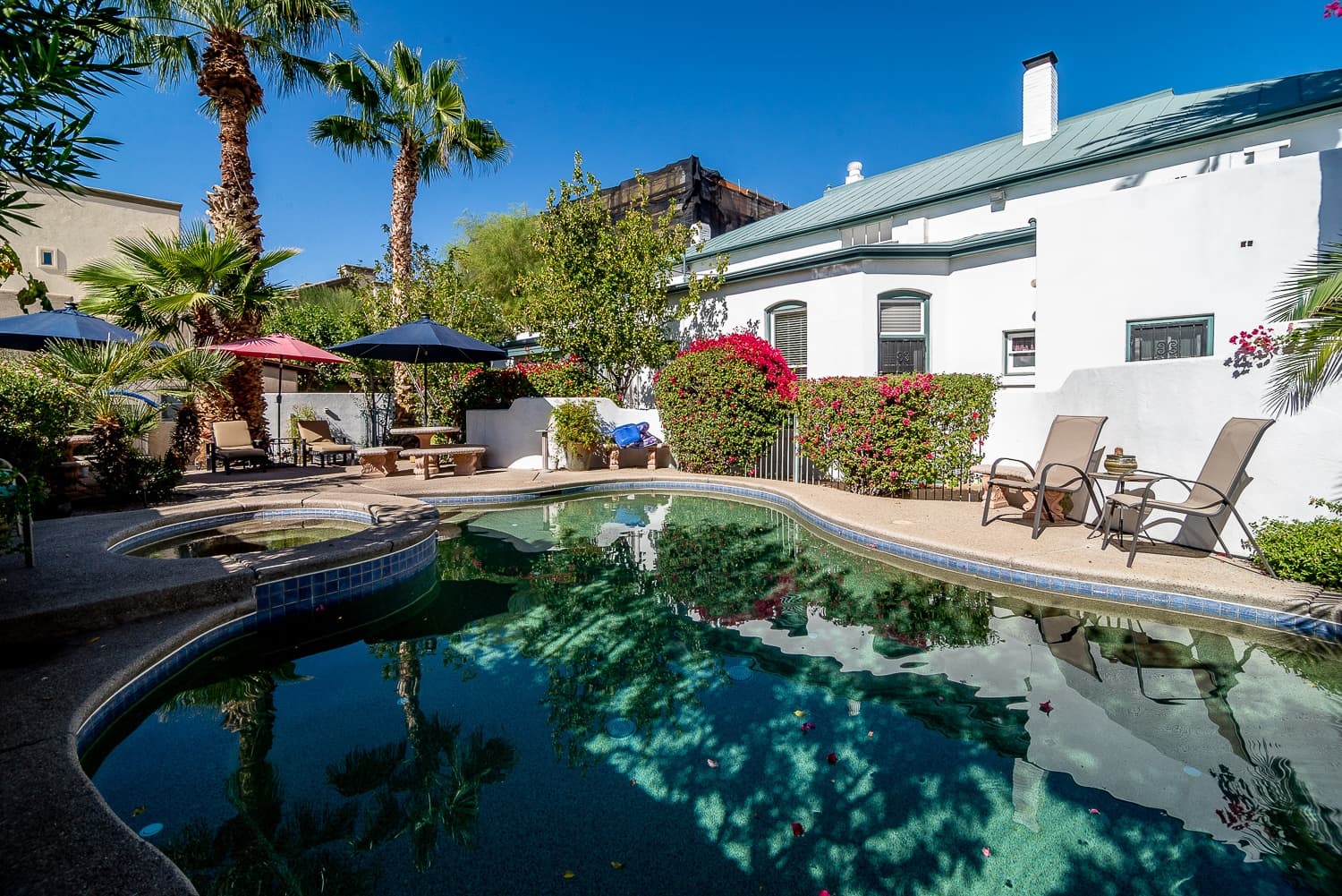 A serene pool area surrounded by palm trees and colorful flowers, featuring lounge chairs and shaded seating.