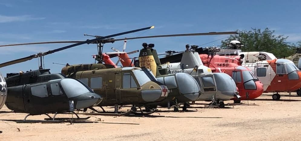 A row of various helicopters parked on dry ground under a clear blue sky. A row of various helicopters parked on dry ground under a clear blue sky.