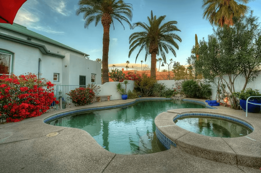 A serene backyard pool surrounded by vibrant flowers and palm trees.