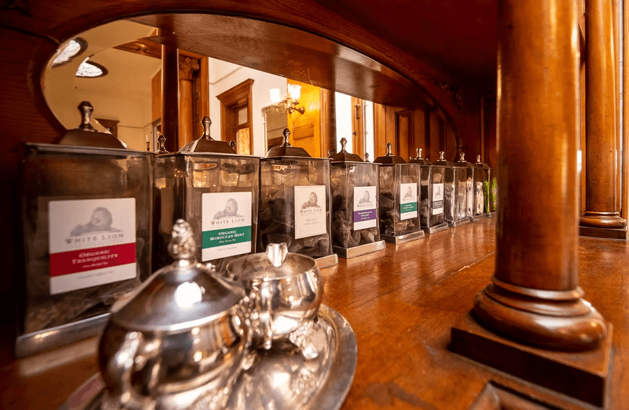 A wooden display featuring labeled tea canisters and a polished silver teapot.
