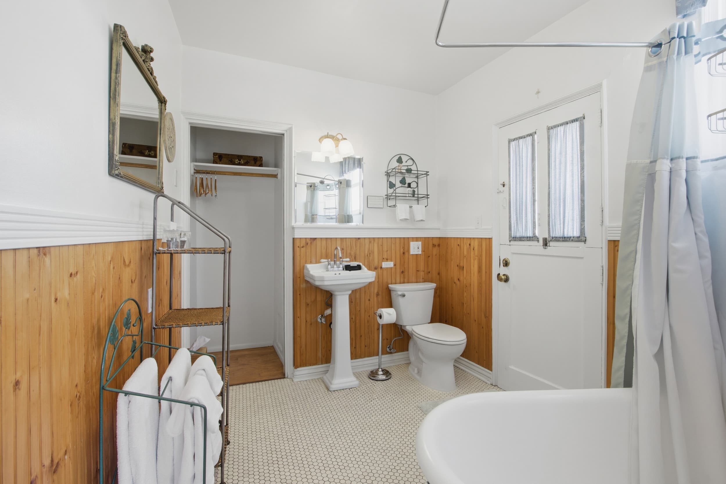 A bright, stylish bathroom featuring a white tub, pedestal sink, toilet, and wooden accents.