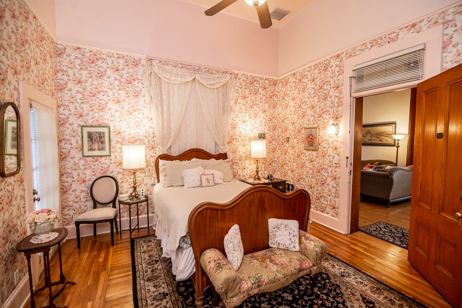 A cozy bedroom with floral wallpaper, a wooden bed, and warm lighting.