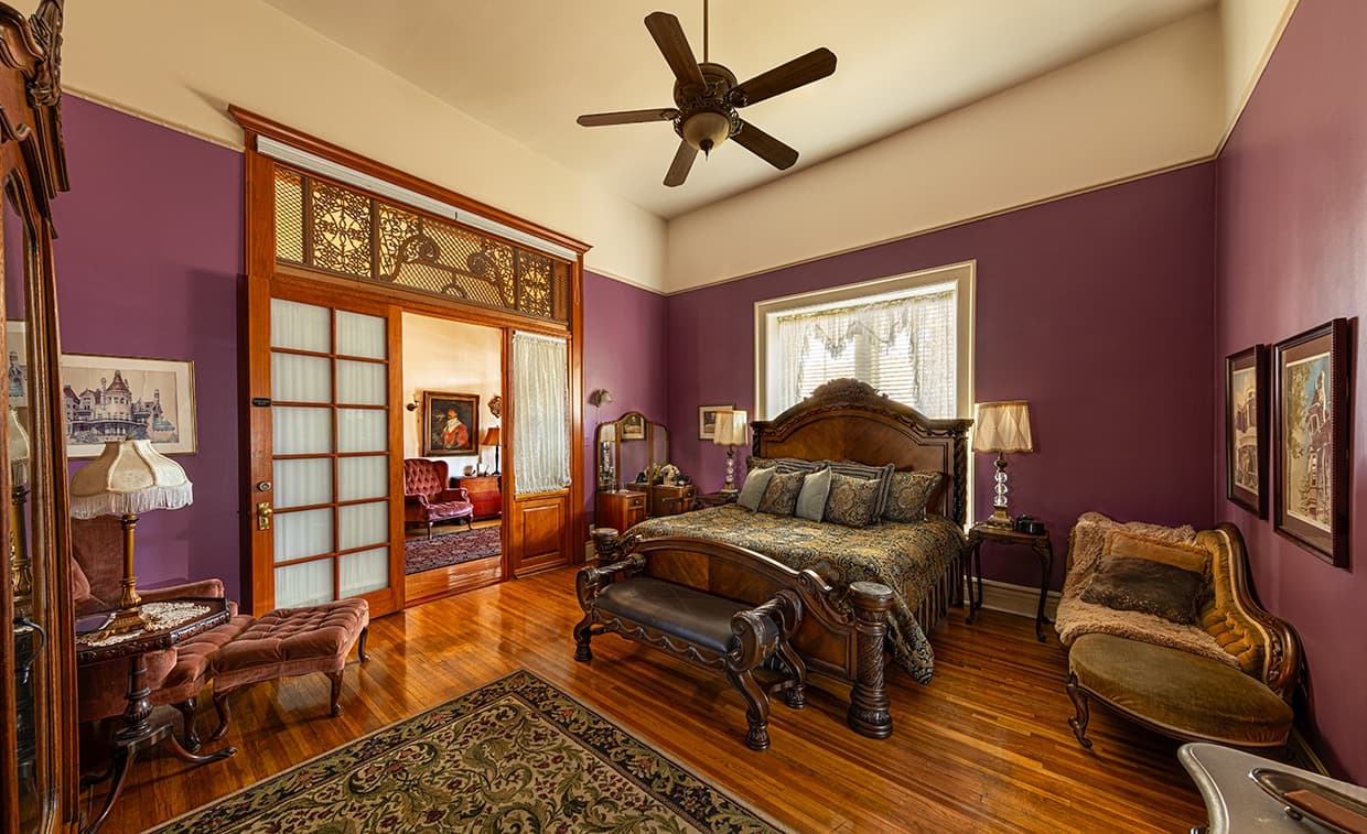 A cozy bedroom featuring a large bed, purple walls, wooden furniture, and a ceiling fan. A cozy bedroom featuring a large bed, purple walls, wooden furniture, and a ceiling fan.
