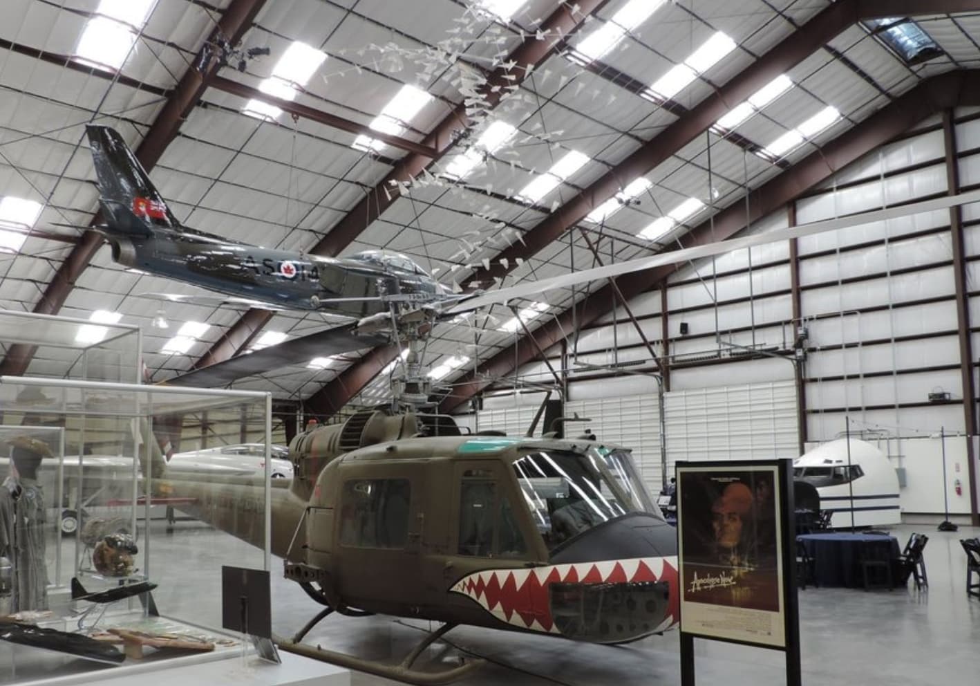 A military helicopter and an airplane are displayed in a large aviation museum hangar.