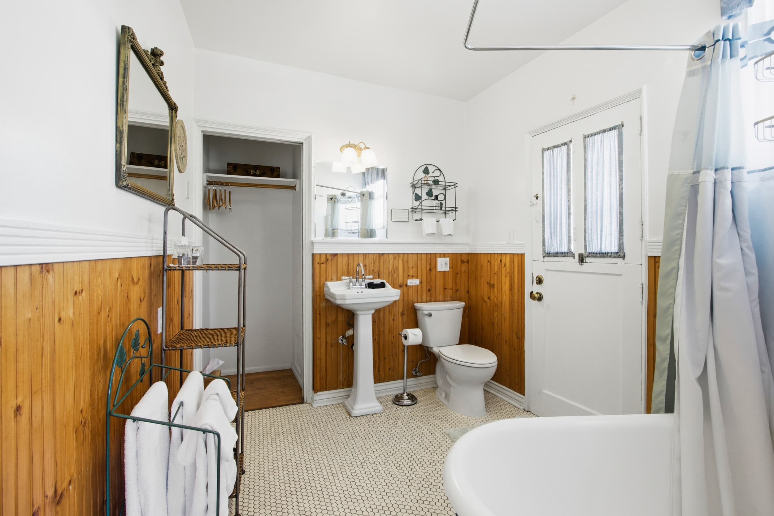 A bright and spacious bathroom with wooden accents, a pedestal sink, and a clawfoot tub.