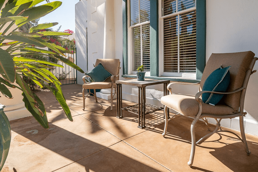 A sunny porch featuring two chairs, a small table, and a potted plant.
