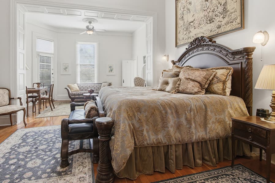 A beautifully decorated bedroom featuring an elegant bed, vintage furniture, and large windows allowing natural light.