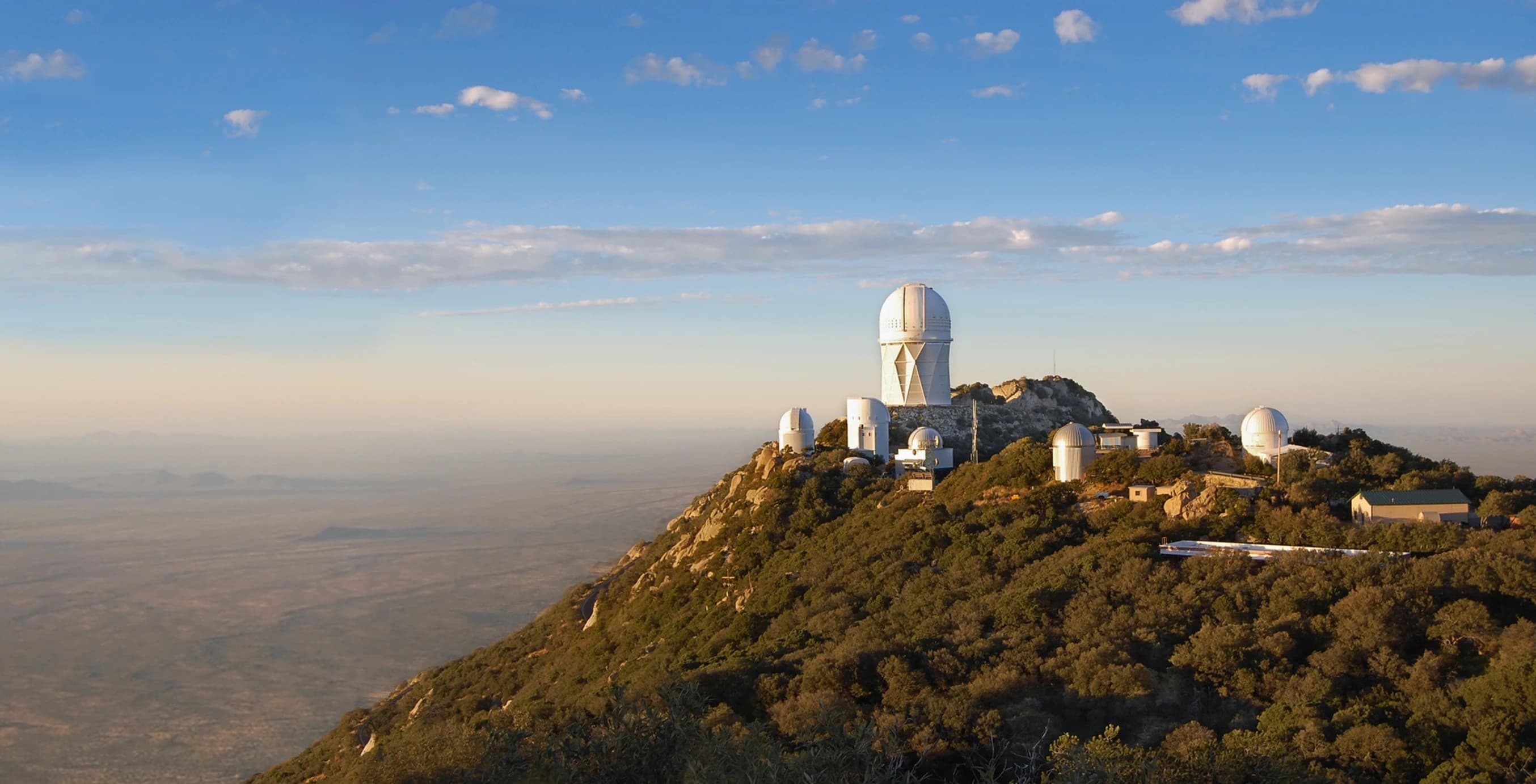 A panoramic view of observatories on a mountain under a clear blue sky. A panoramic view of observatories on a mountain under a clear blue sky.