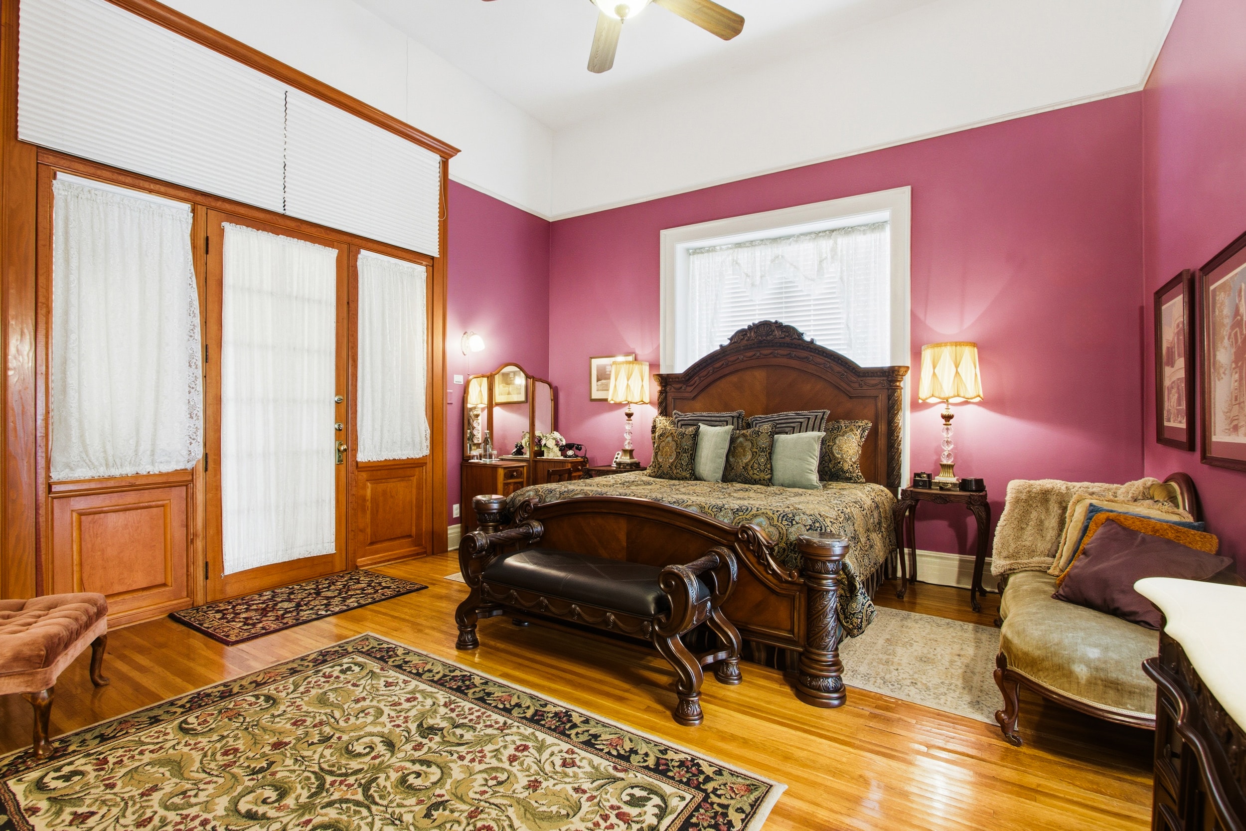 A cozy bedroom featuring a dark wood bed, warm lighting, and rich purple walls.