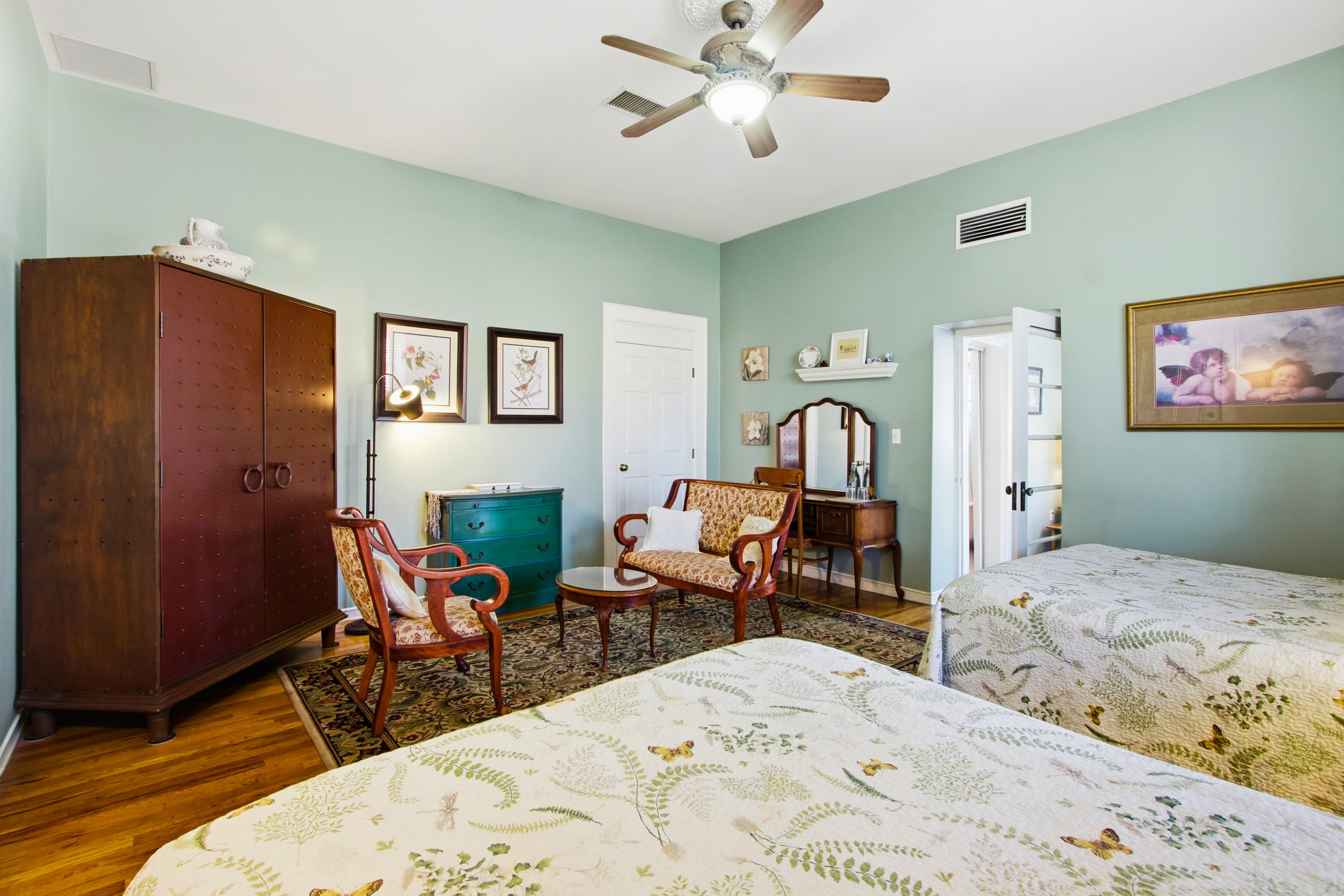 A cozy bedroom featuring two beds, vintage furniture, and light green walls.