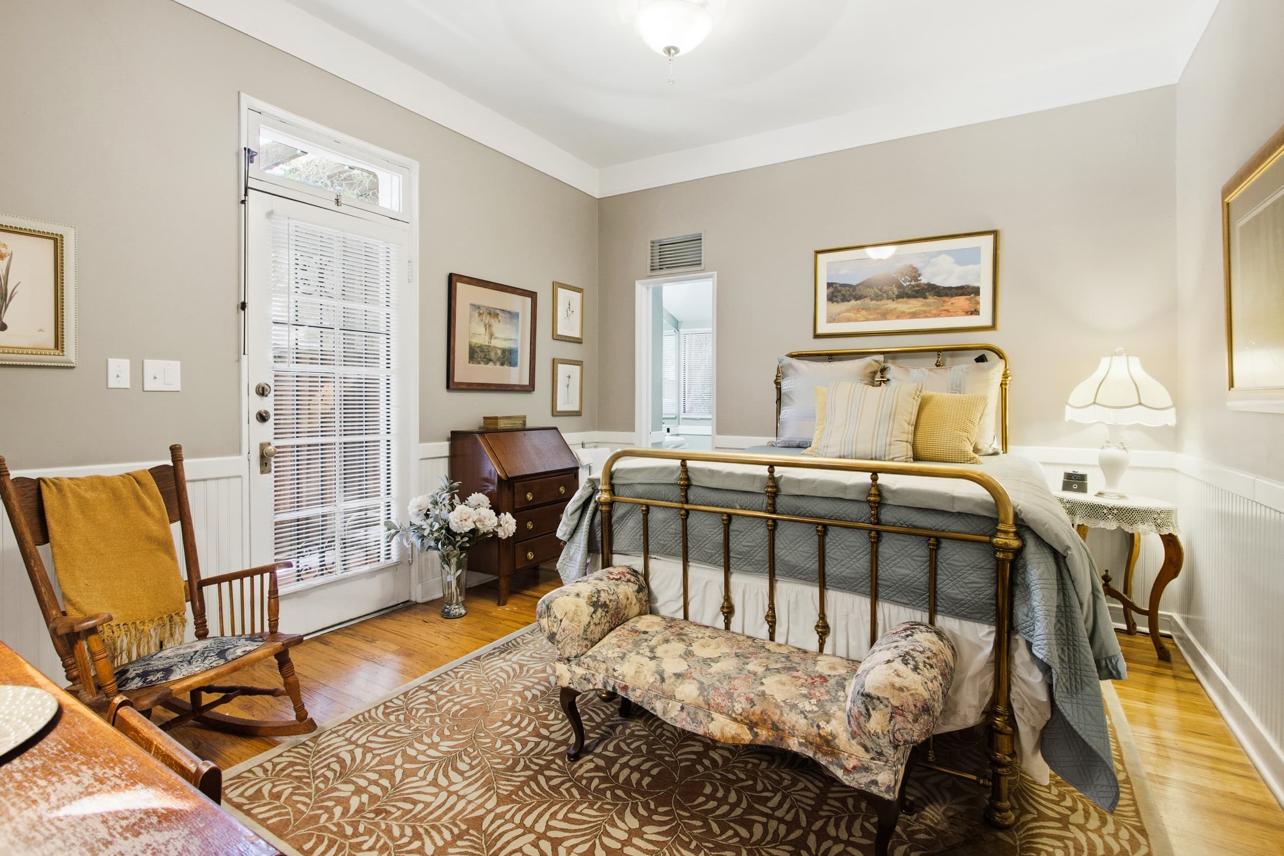 Cozy bedroom featuring a brass bed, floral bench, and wooden furniture in soft, neutral tones.