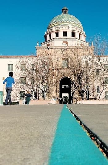 A view of a building with a dome and an archway, featuring a blue line on the pavement and people walking. A view of a building with a dome and an archway, featuring a blue line on the pavement and people walking.